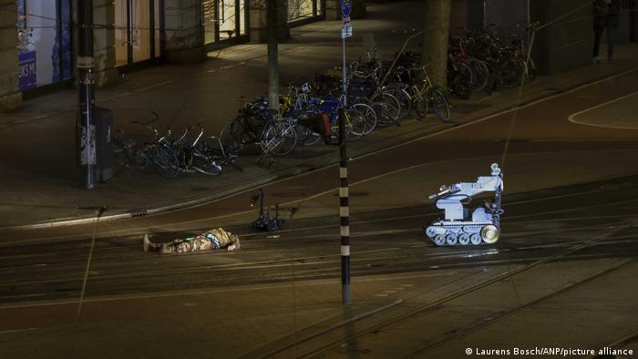 Een man in camouflage ligt naast een politierobot op straat