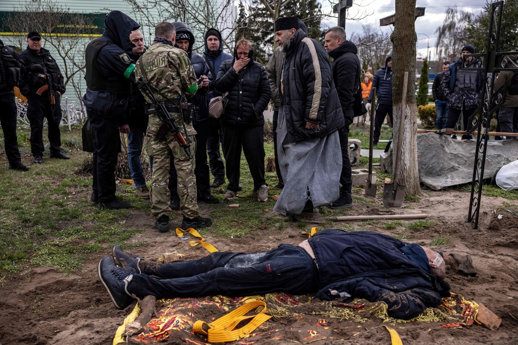 Een priester en zijn familieleden hebben contact met het lichaam van de burgemeester van Gostomel, Yuri Prilypko, die op 12 april 2022 is begraven in de buurt van een kerk in het dorp Gostomel, in de regio Kiev.