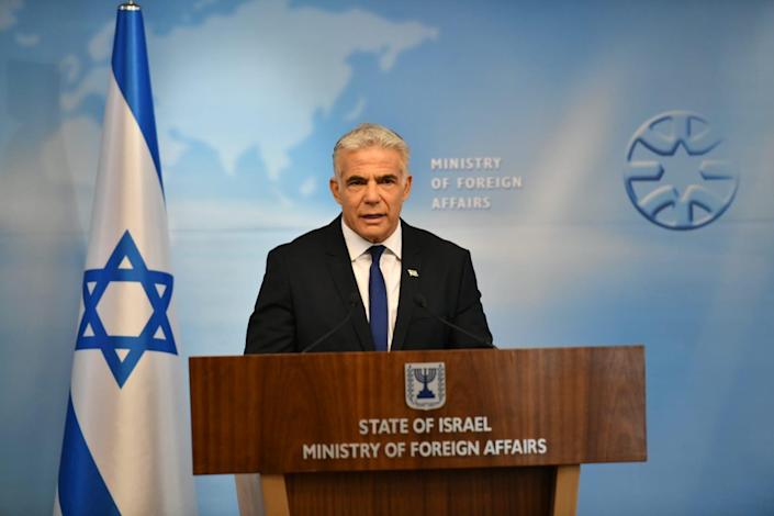 De Israëlische minister van Buitenlandse Zaken Yair Lapid op een podium naast de Israëlische vlag, achter hem staat het ministerie van Buitenlandse Zaken op de muur gedrukt.