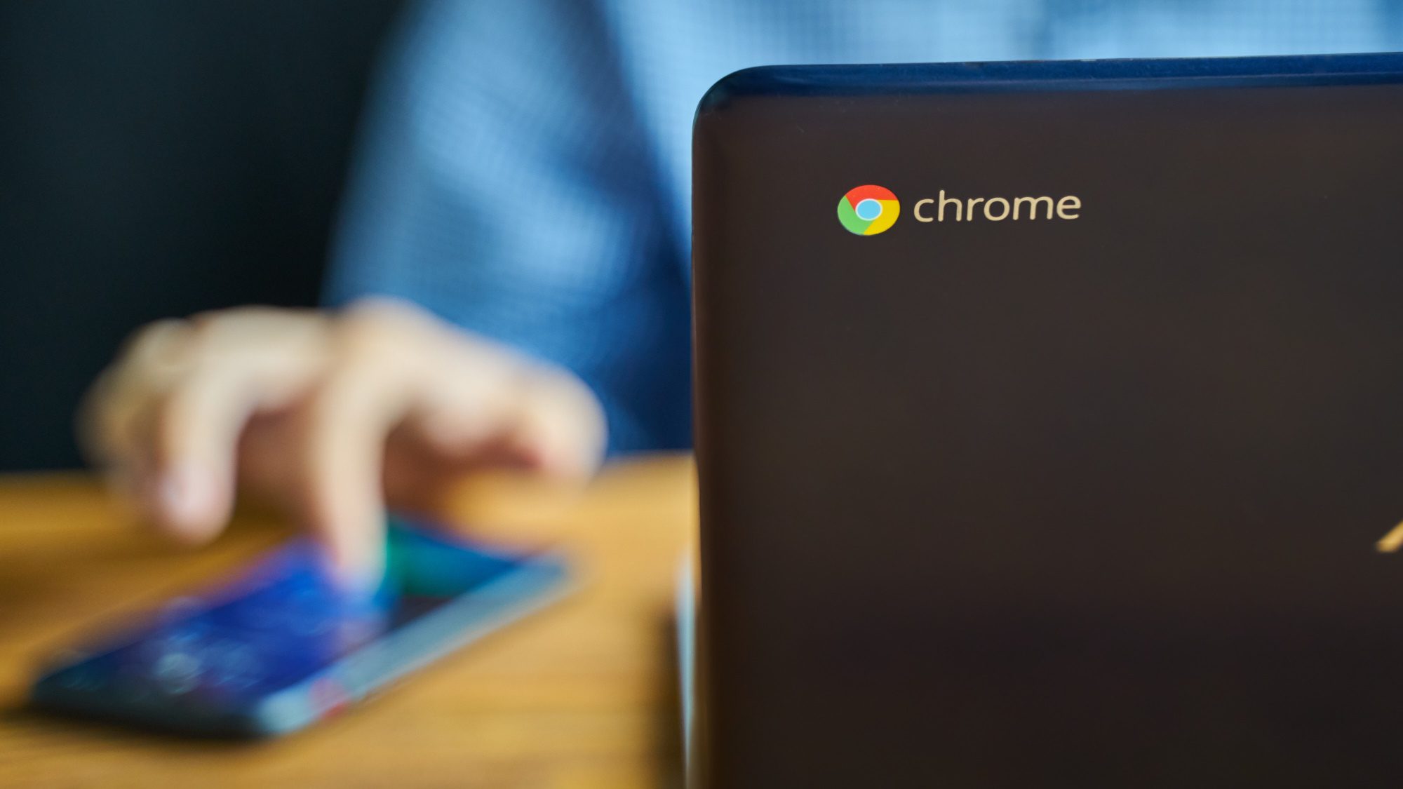 Chrome-logo op de achterkant van een Chromebook met een onscherpe man die eraan werkt