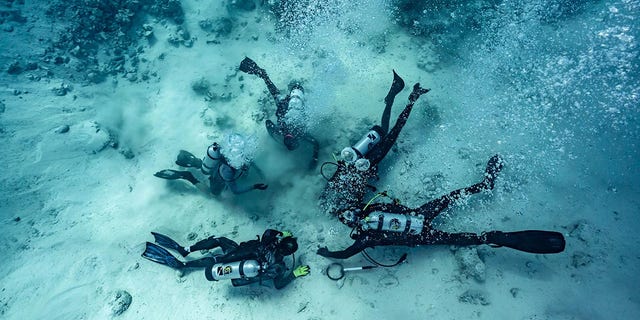 Duikers worden getoond op zoek naar schatten begraven op de bodem van de zee - de plaats van een scheepswrak in de Bahama's.