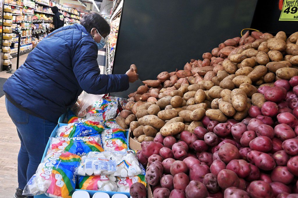 Een vrouw deelt aardappelen uit in een kruidenierswinkel.