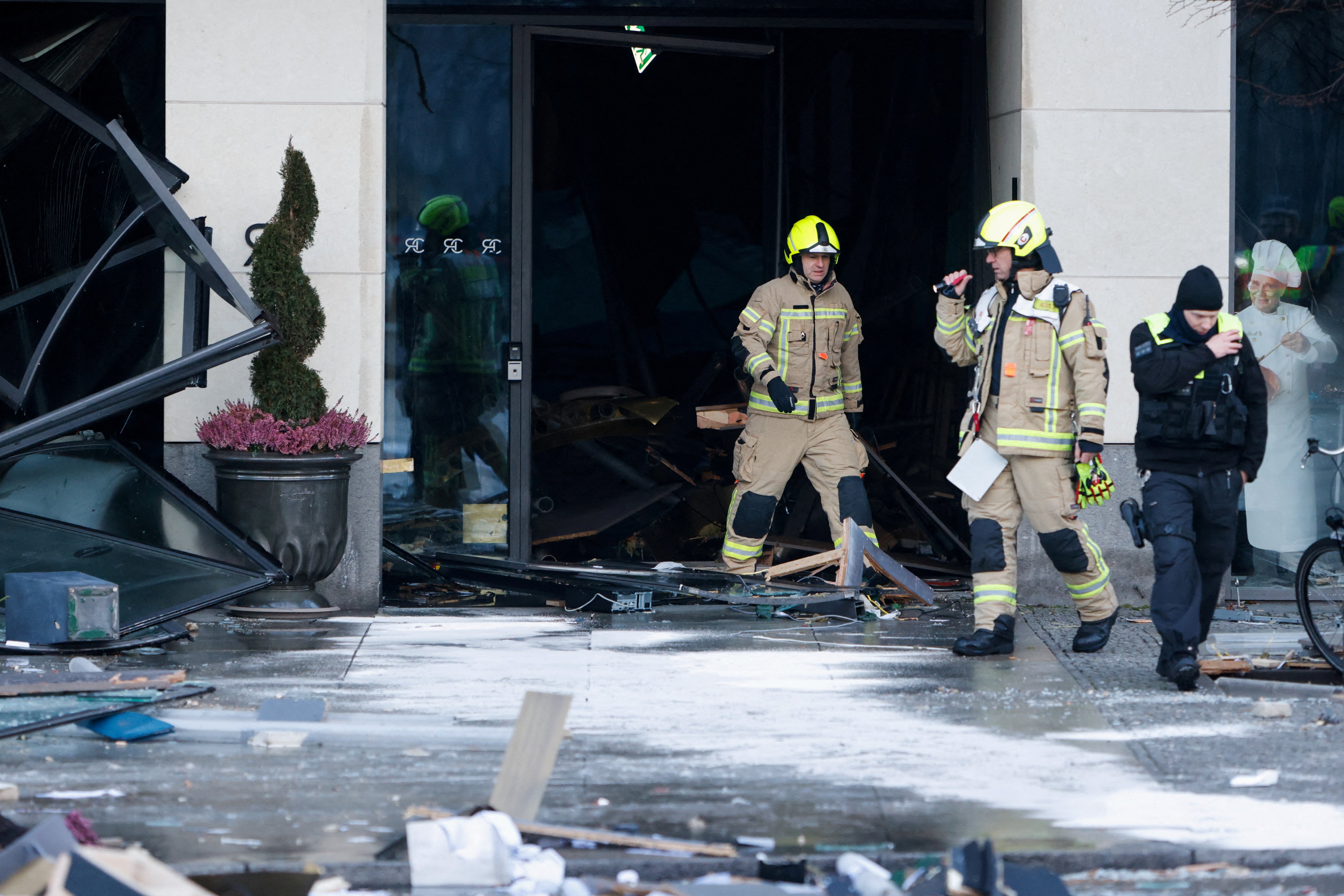 Hulpverleners staan ​​buiten een gebouw, met veel gebroken glas en puin om hen heen.